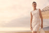 Woman in a white lace dress standing on a beach with an umbrella in the background