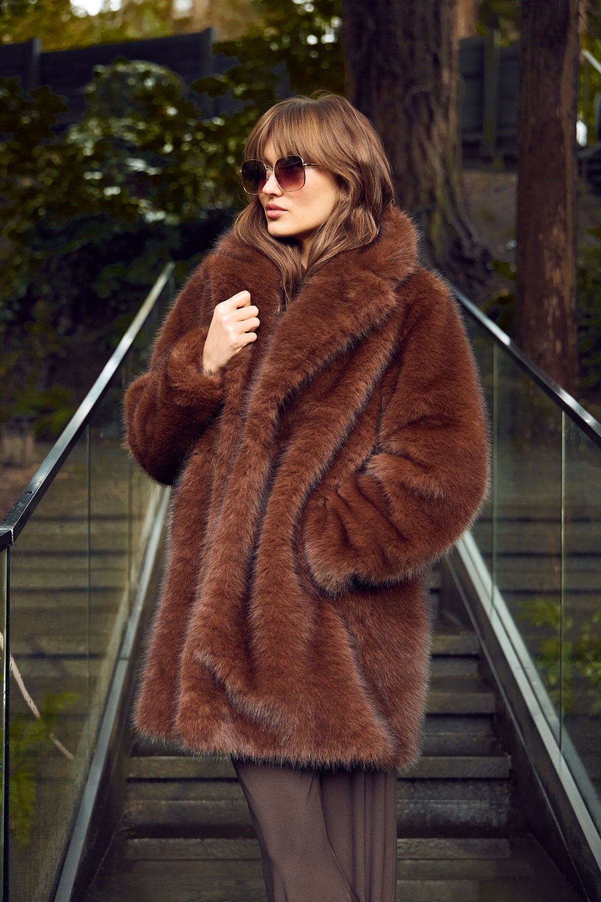 Woman wearing a brown fur coat and sunglasses on an outdoor staircase.