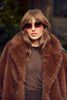 Woman wearing a brown fur coat and sunglasses with a blurred natural background