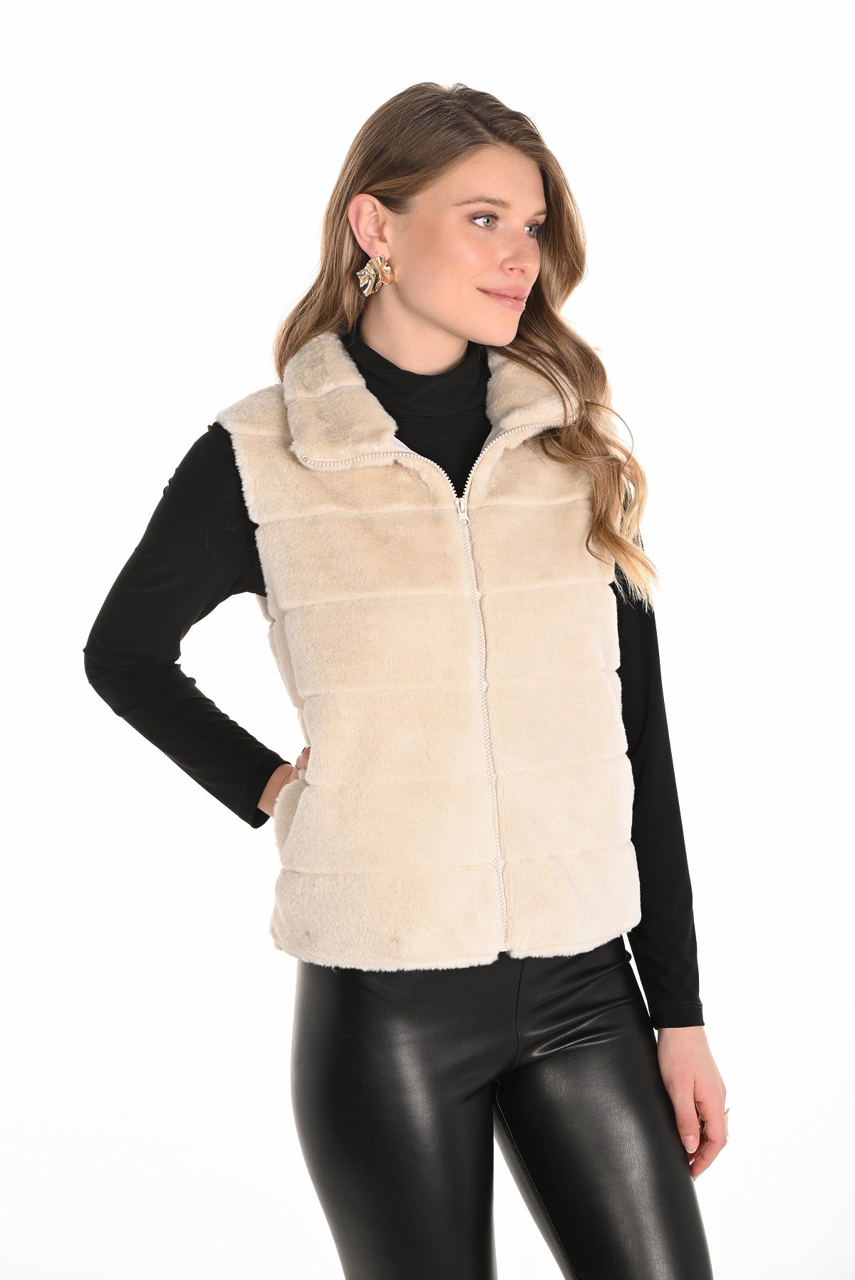 Woman wearing a beige vest over a black long-sleeve shirt and black pants on a white background