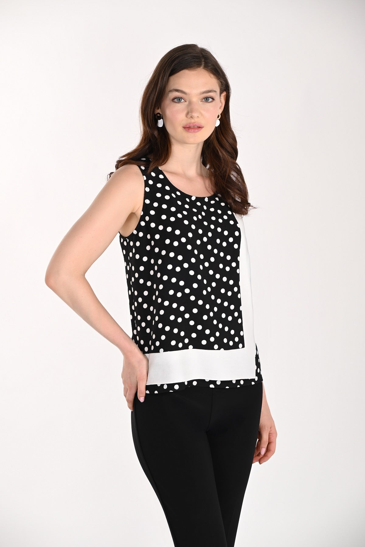 Woman wearing a black and white polka dot sleeveless top with a white shirt underneath on a white background