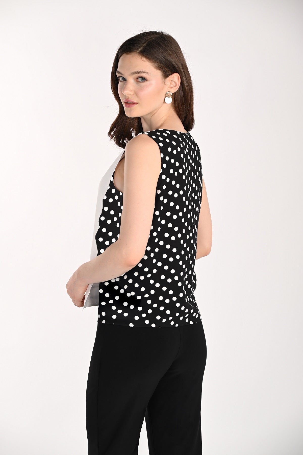 Woman wearing a black sleeveless top with white polka dots and black pants on a white background