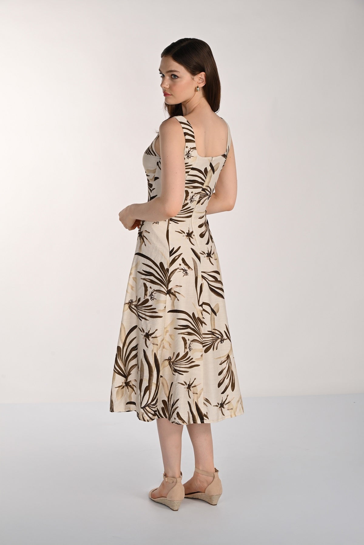 Woman wearing a sleeveless dress with leaf pattern on a plain background