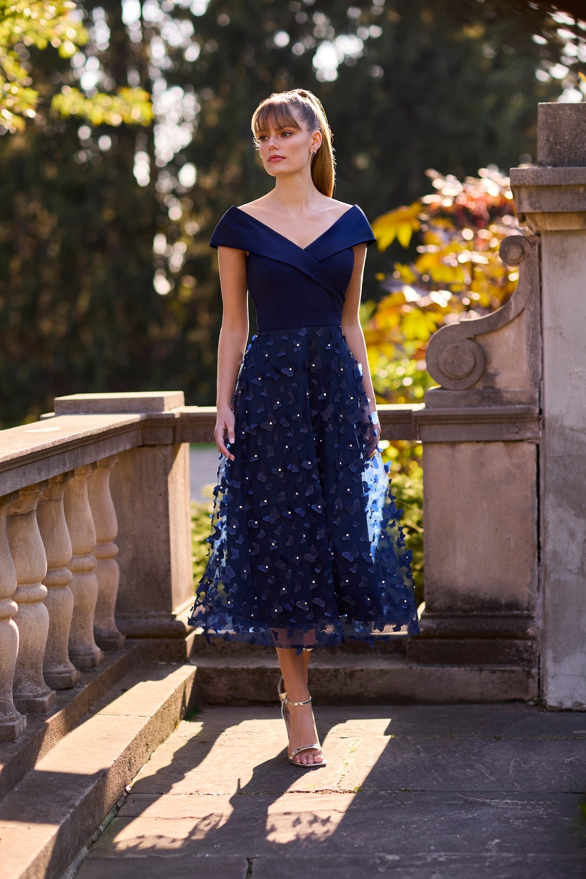 Woman in a blue dress standing on stone steps with greenery in the background