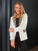 Woman wearing a white blazer with leopard print accents against a black background