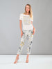 Woman wearing a white top with floral embellishments and floral pants on a gray background