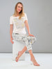 Woman wearing a white t-shirt with floral design and light-colored pants against a gray background