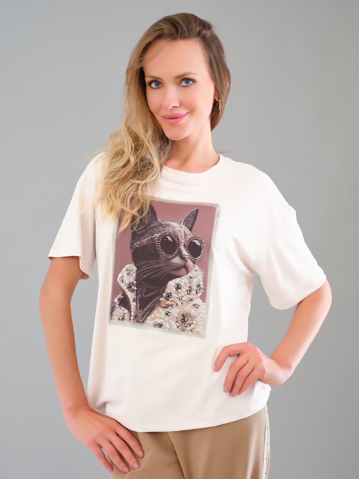 Woman wearing a white t-shirt with a graphic of a cat wearing sunglasses on a gray background