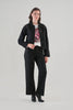 A woman modeling a black cropped jacket with silver rhinestone embellishments on the shoulders and sides, paired with black wide-leg trousers, a white graphic t-shirt, and black ankle boots, against a light gray studio background.