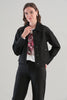 A woman modeling a black cropped denim jacket with silver rhinestone embellishments on the shoulders and sides, worn over a white graphic t-shirt and black pants, against a light gray studio background.