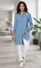 Woman wearing a blue denim shirt and white pants in a blurred indoor setting