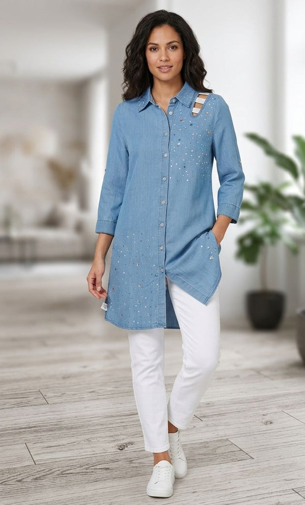 Woman wearing a blue denim shirt and white pants in a blurred indoor setting