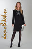 Woman wearing a black dress with a floral design and white accents, standing against a gray background. Brand 'Jane & John' visible.