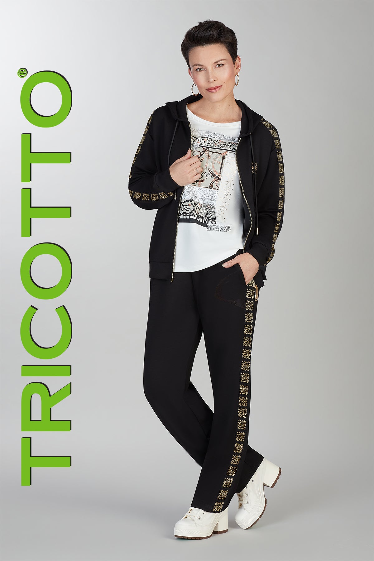 Person wearing a black tracksuit with gold accents and white sneakers, standing against a gray background with 'TRICOTTO' branding