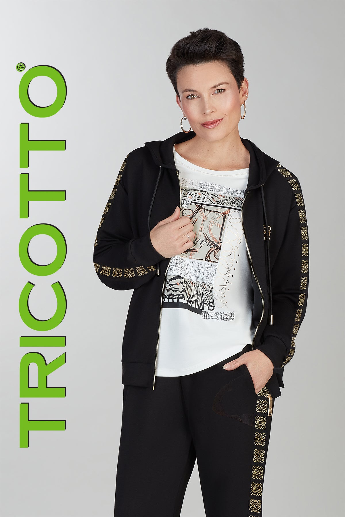 Person wearing a black hoodie and pants with decorative elements, holding a phone, on a gray background with 'TRICOTTO' branding.