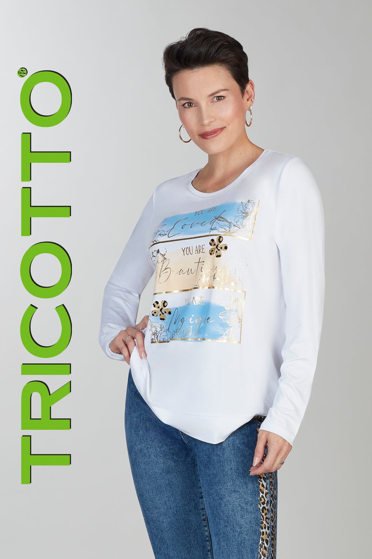 Woman wearing a white sweater with a colorful design, standing against a gray background with 'TRICOTTO' branding.