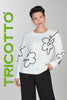 Woman wearing a white sweater with black abstract designs on a gray background, featuring the brand 'Tricotto'.
