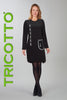 Woman wearing a black dress with white text and a pocket, standing against a gray background with 'TRICOTTO' branding.