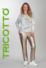 Woman wearing a patterned top and metallic pants with 'TRICOTTO' branding on a gray background