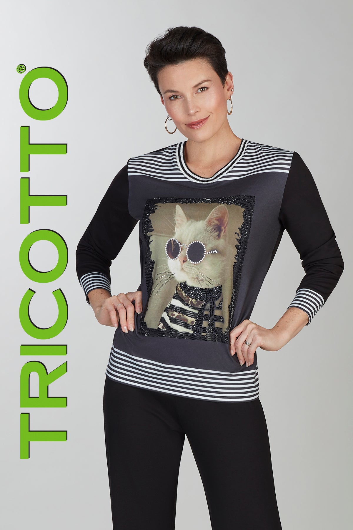 Woman wearing a black and white striped shirt with a cat graphic, branded 'Tricotto'.