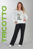 Woman wearing a white sweater with a graphic design and black pants, standing against a gray background with 'TRICOTTO' branding.