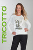 Woman wearing a white sweater with a graphic design, standing against a plain background with 'TRICOTTO' branding.
