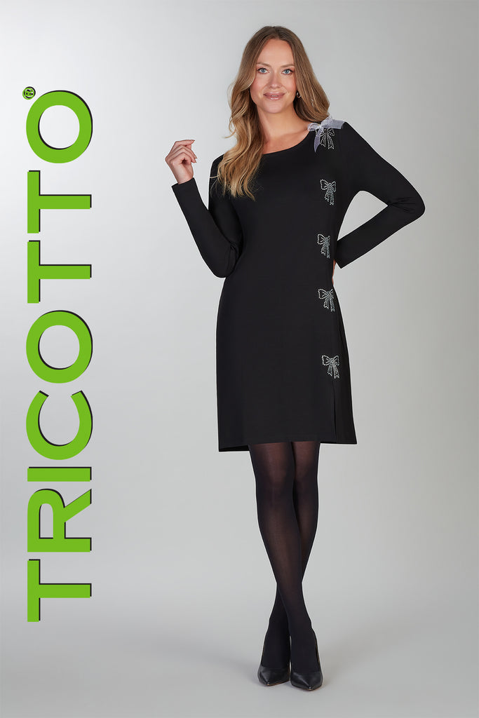 Woman wearing a black dress with butterfly details, standing against a white background with 'TRICOTTO' branding.